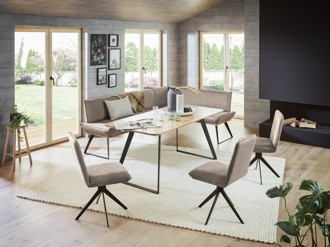 Moderne Esszimmer-Eckbankgruppe mit Tisch und Stühlen in einem hellen Raum mit großen Fenstern, seitliche Perspektive.