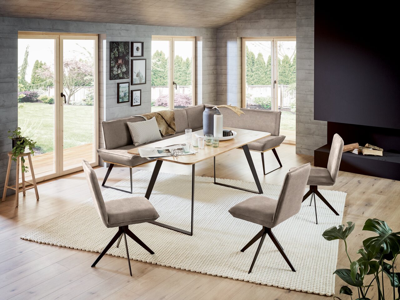 Moderne Esszimmer-Eckbankgruppe mit Tisch und Stühlen in einem hellen Raum mit großen Fenstern, seitliche Perspektive.