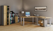Modernes Büro-Set mit L-förmigem Schreibtisch in Holzoptik und weißem Metallgestell, Rollcontainer mit Schubladen sowie Aktenschrank mit offenen Fächern und Holztüren; Ansicht aus schräger Frontperspektive von links.