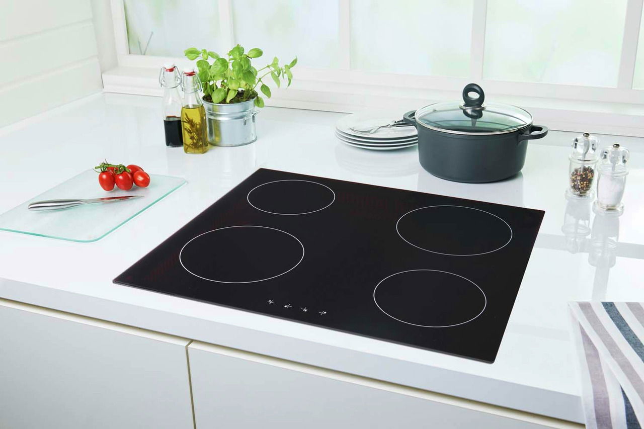 Moderne schwarze Glaskeramik-Kochfläche mit vier Kochzonen, umgeben von einer stilvollen weißen Küchenzeile. Perspektive von oben.