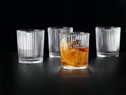 Vier elegante, geriffelte Gläser auf einem dunklen Tisch, eines mit Getränk gefüllt, aus seitlicher Perspektive.