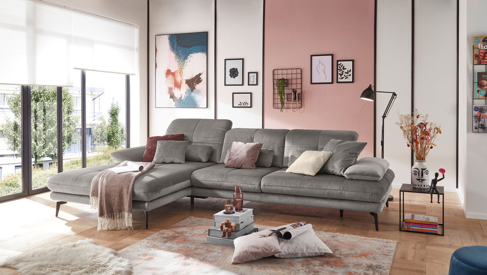 Graue Rundecke (L) in modernem Wohnzimmer, seitliche Perspektive, dekoriert mit Kissen und Decke, umgeben von stilvollen Wandbildern und großen Fenstern.