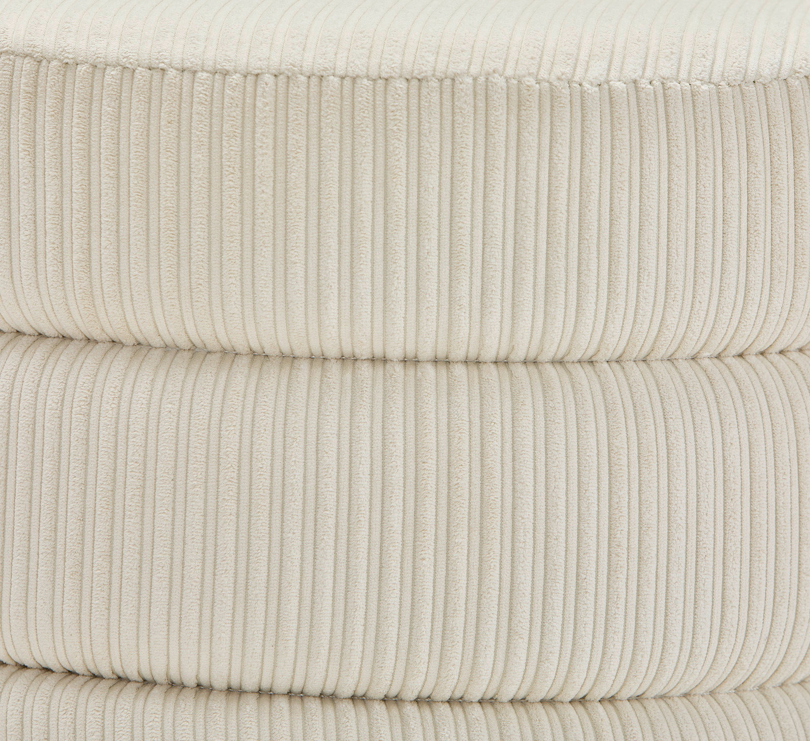 Nahaufnahme eines cremefarbenen, gerippten Hockers aus Stoff, seitliche Perspektive