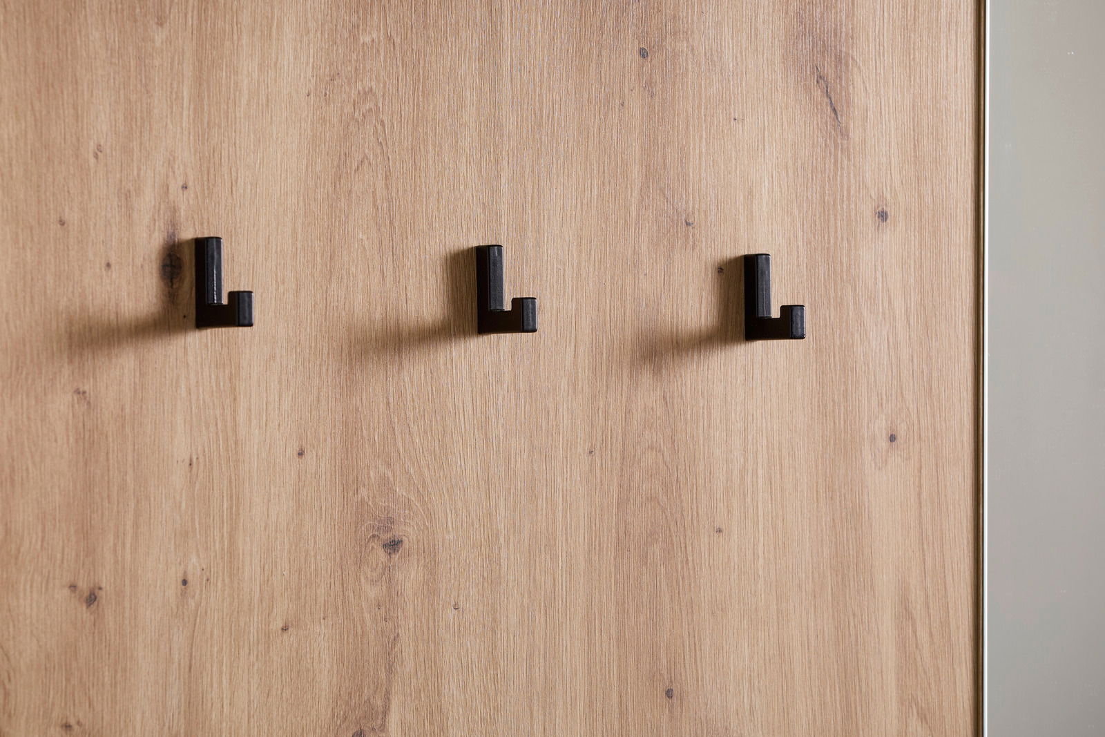 Nahaufnahme einer Kompaktgarderobe mit drei schwarzen Haken auf einer Holzoberfläche, seitliche Perspektive.