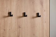 Nahaufnahme einer Kompaktgarderobe mit drei schwarzen Haken auf einer Holzoberfläche, seitliche Perspektive.