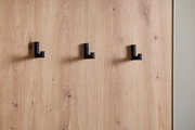 Nahaufnahme einer Kompaktgarderobe mit drei schwarzen Haken auf einer Holzoberfläche, seitliche Perspektive.