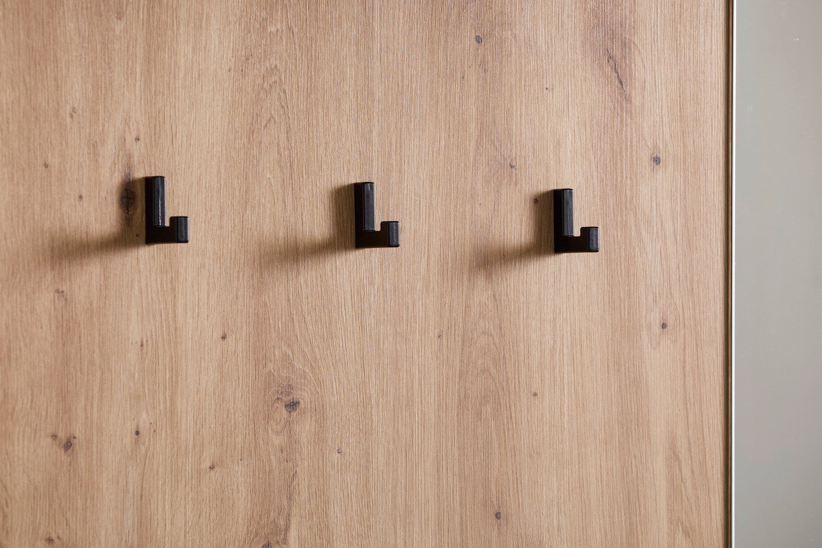 Nahaufnahme einer Kompaktgarderobe mit drei schwarzen Haken auf einer Holzoberfläche, seitliche Perspektive.