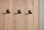 Nahaufnahme einer Kompaktgarderobe mit drei schwarzen Haken auf einer Holzoberfläche, seitliche Perspektive.