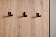 Nahaufnahme einer Kompaktgarderobe mit drei schwarzen Haken auf einer Holzoberfläche, seitliche Perspektive.