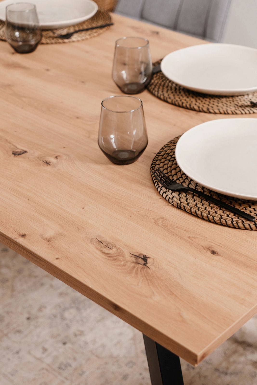 Nahaufnahme eines Esstisches aus Holz mit gedecktem Tisch, inklusive Gläsern und Tellern, aus seitlicher Perspektive.