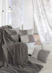 Gemütliche Chenille Wohndecke in Grau auf einem Sofa drapiert, umgeben von passenden Kissen in einem modernen Wohnzimmer.