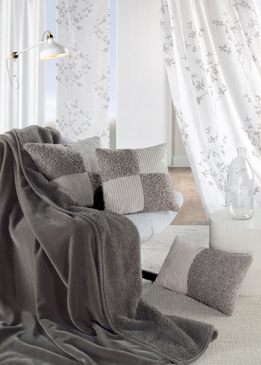 GÖZZE Wohndecke PAULA Gemütliche Chenille Wohndecke in Grau auf einem Sofa drapiert, umgeben von passenden Kissen in einem modernen Wohnzimmer.