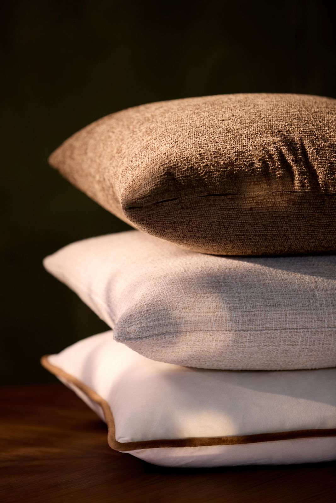 Drei übereinander gestapelte Kissen in verschiedenen Texturen und Farben, seitliche Perspektive