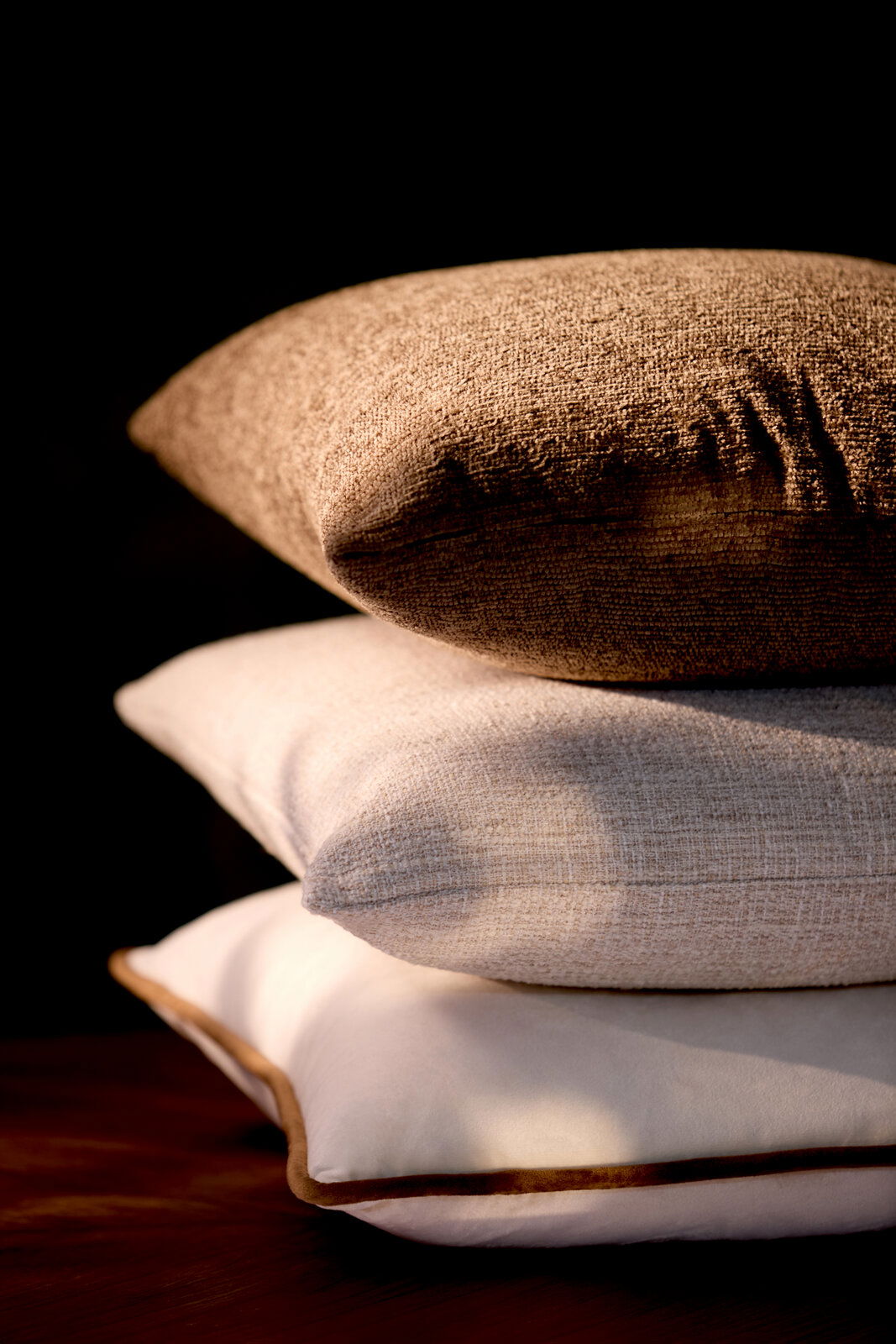 Drei übereinander gestapelte Kissen in verschiedenen Texturen und Farben, seitliche Perspektive