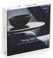 Verpackung des Stressless Swing Table, seitliche Perspektive, zeigt einen Tisch mit einer Schale darauf.