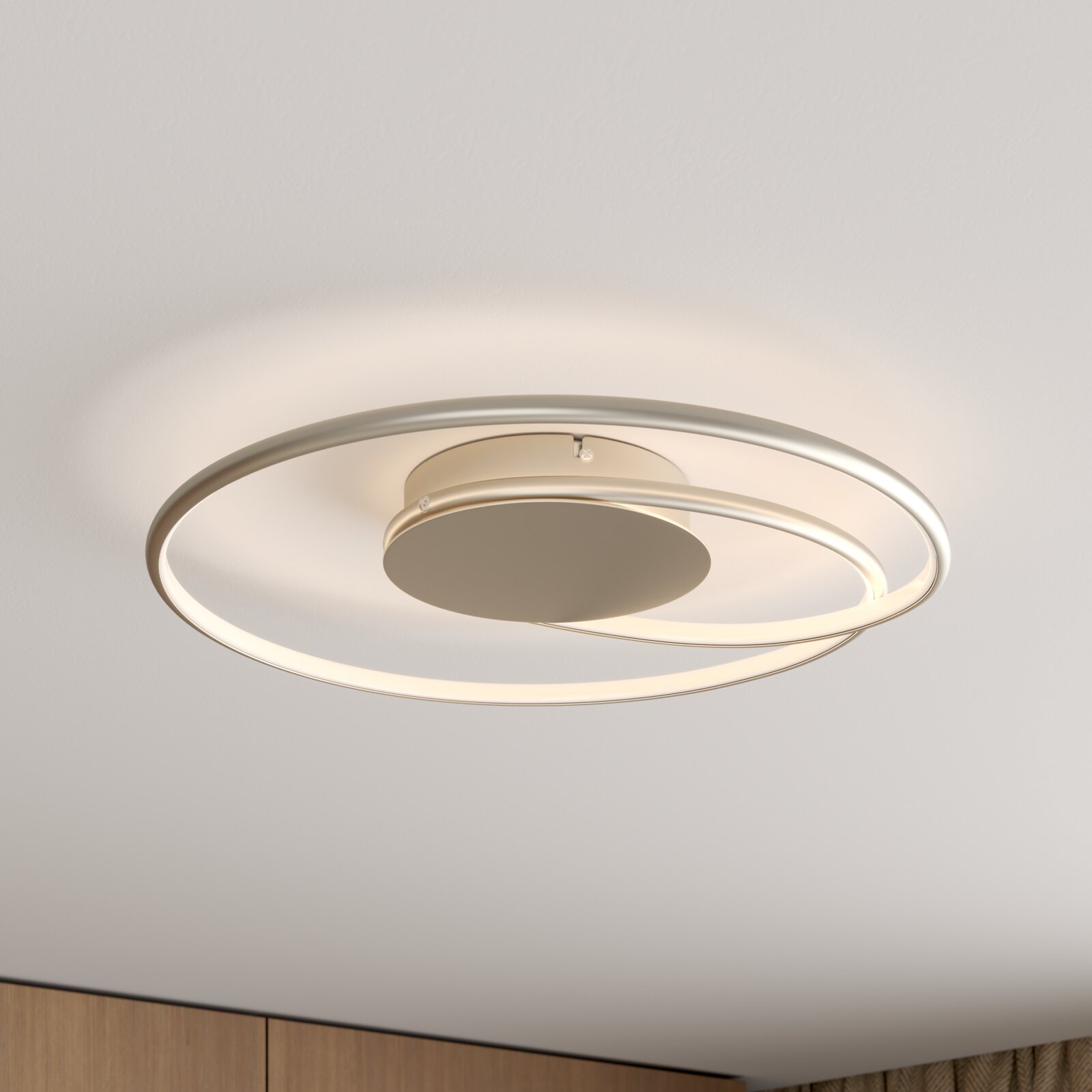 Moderne runde LED-Deckenleuchte mit zwei ringförmigen Lichtbändern in Metalloptik, warmweiß leuchtend, Unteransicht leicht schräg von unten an der Decke