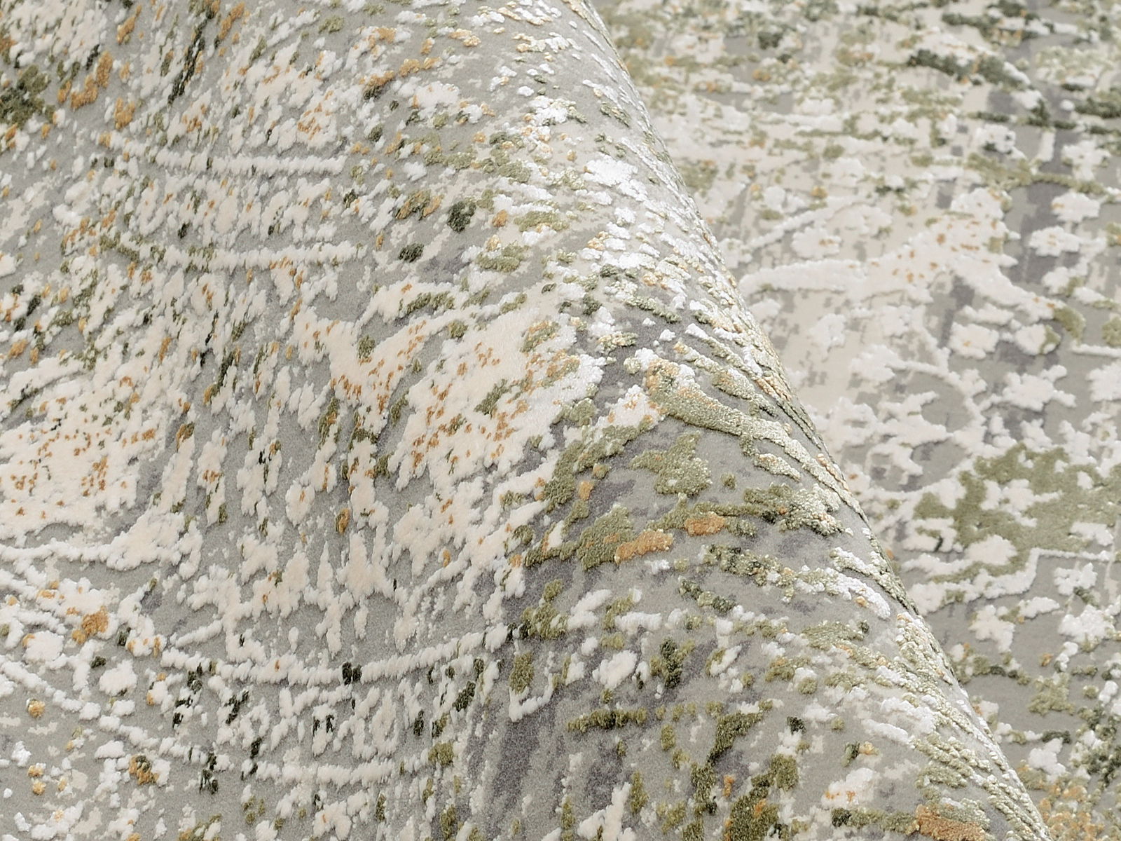 Nahaufnahme eines Designer-Teppichs mit abstraktem Muster in Grün-, Grau- und Beigetönen, perspektivisch von der Seite aufgenommen.