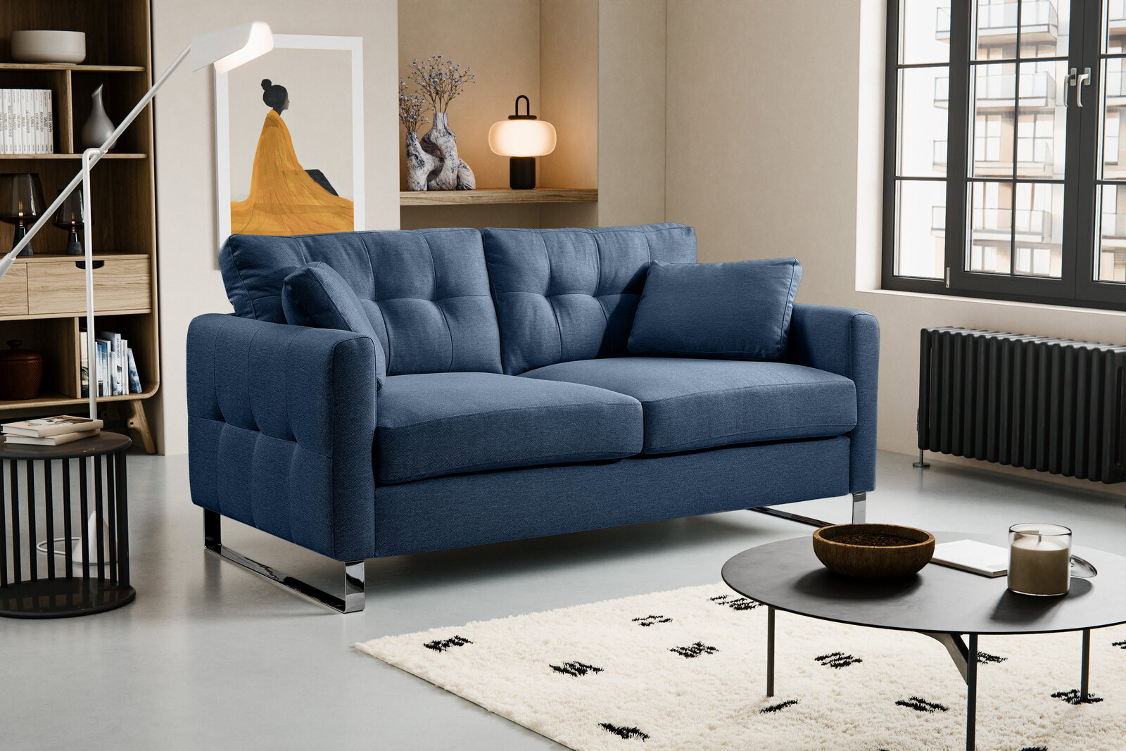 Blaues, modern gepolstertes 2-Sitzer-Sofa mit Steppung, zwei Kissen und verchromten Metallfüßen im Wohnzimmer, schräg von vorne links fotografiert.
