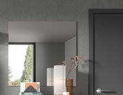 Moderner rechteckiger Wandspiegel in einem Raum mit grauer Wand, neben einer Tür und Dekorationen, aus seitlicher Perspektive.
