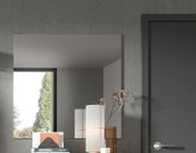 Moderner rechteckiger Wandspiegel in einem Raum mit grauer Wand, neben einer Tür und Dekorationen, aus seitlicher Perspektive.