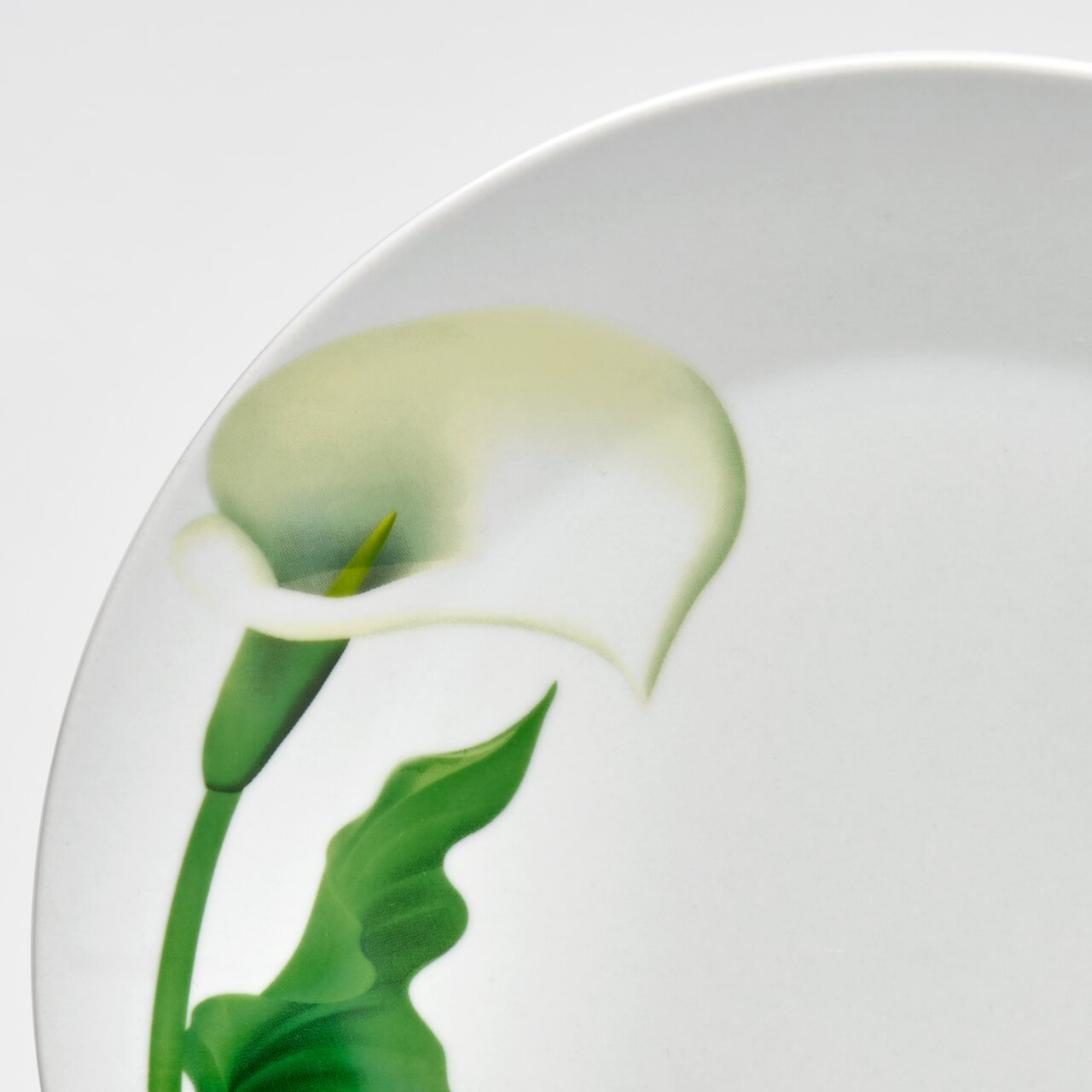 Nahaufnahme eines weißen Porzellantellers mit Calla-Blütenmotiv in Grün und Weiß, schräg von oben fotografiert.