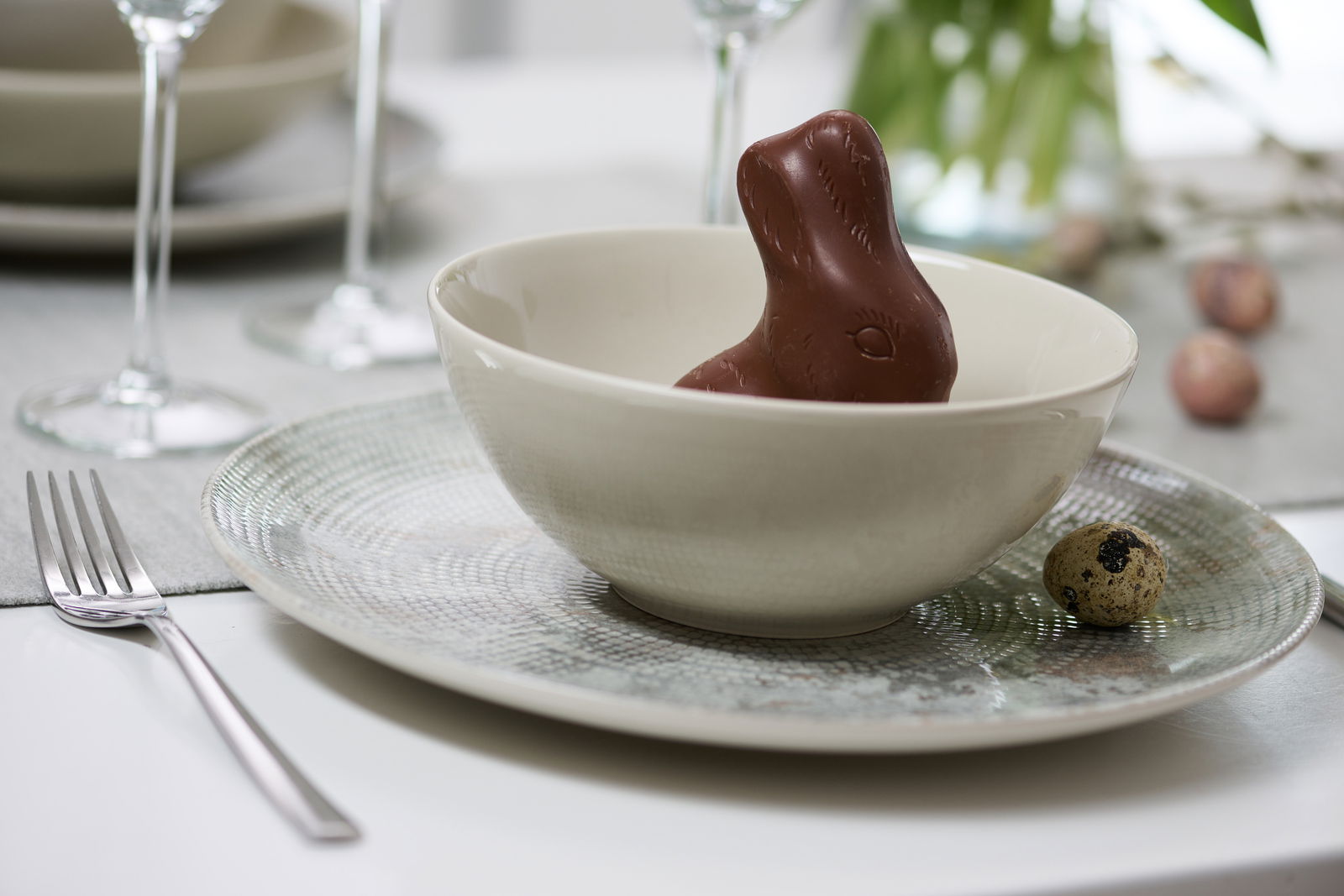 Tiefer Teller mit Perlendesign, darauf eine Schale mit einem Schokoladenhasen, seitliche Perspektive.