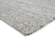 Nahaufnahme eines handgewebten Teppichs in Grautönen, perspektivisch von der Seite aufgenommen.