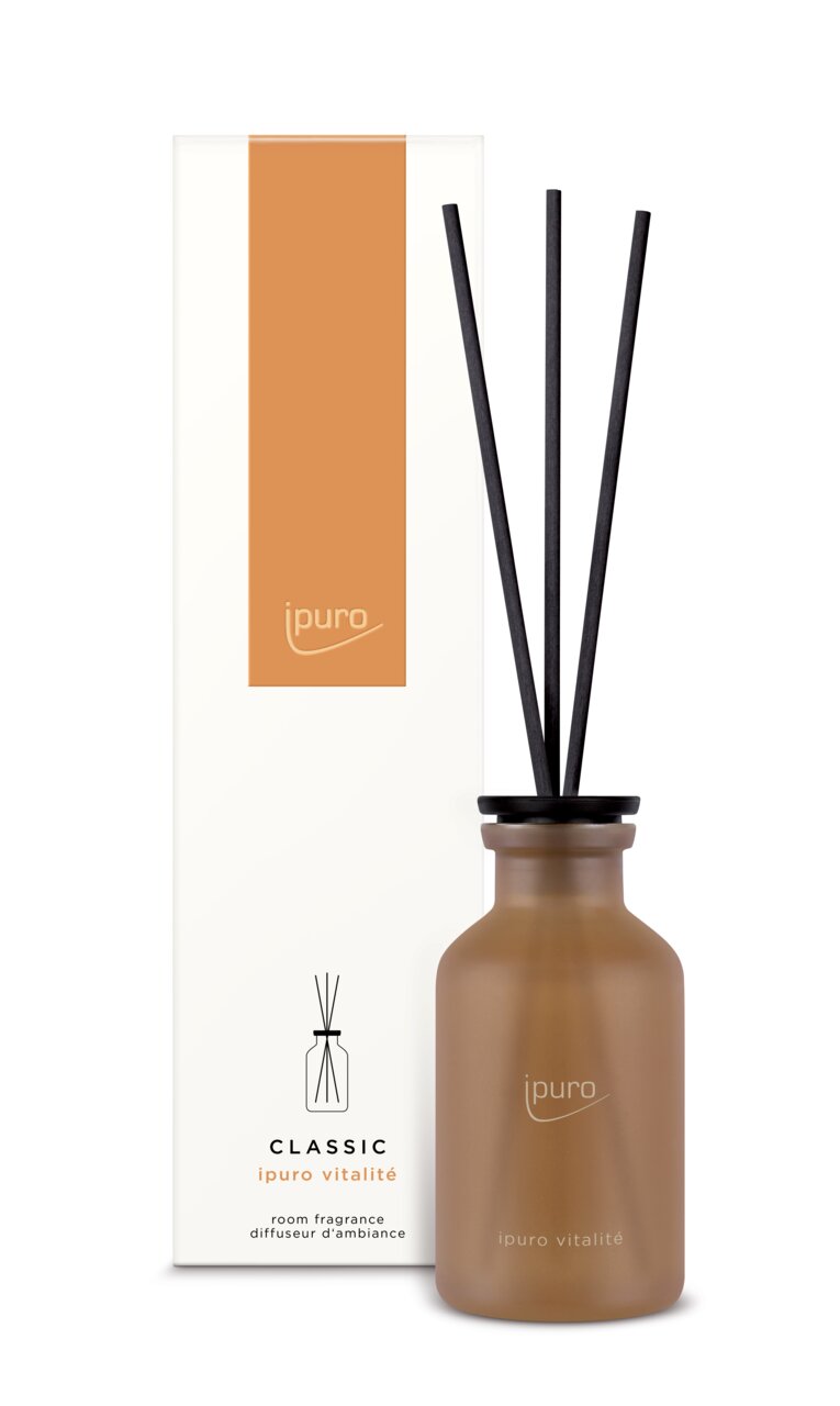 Brauner Raumduft-Diffusor mit schwarzen Stäbchen, vor einer weißen Verpackung mit orangefarbenem Akzent, aus der Frontalperspektive.