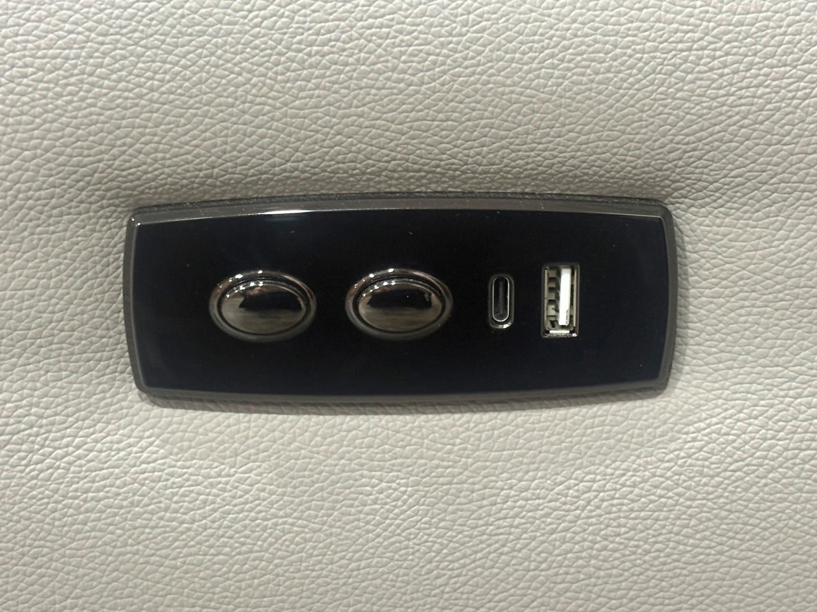 Nahaufnahme eines schwarzen Bedienfelds auf einem hellgrauen Sofa mit zwei Knöpfen und USB-Anschlüssen.
