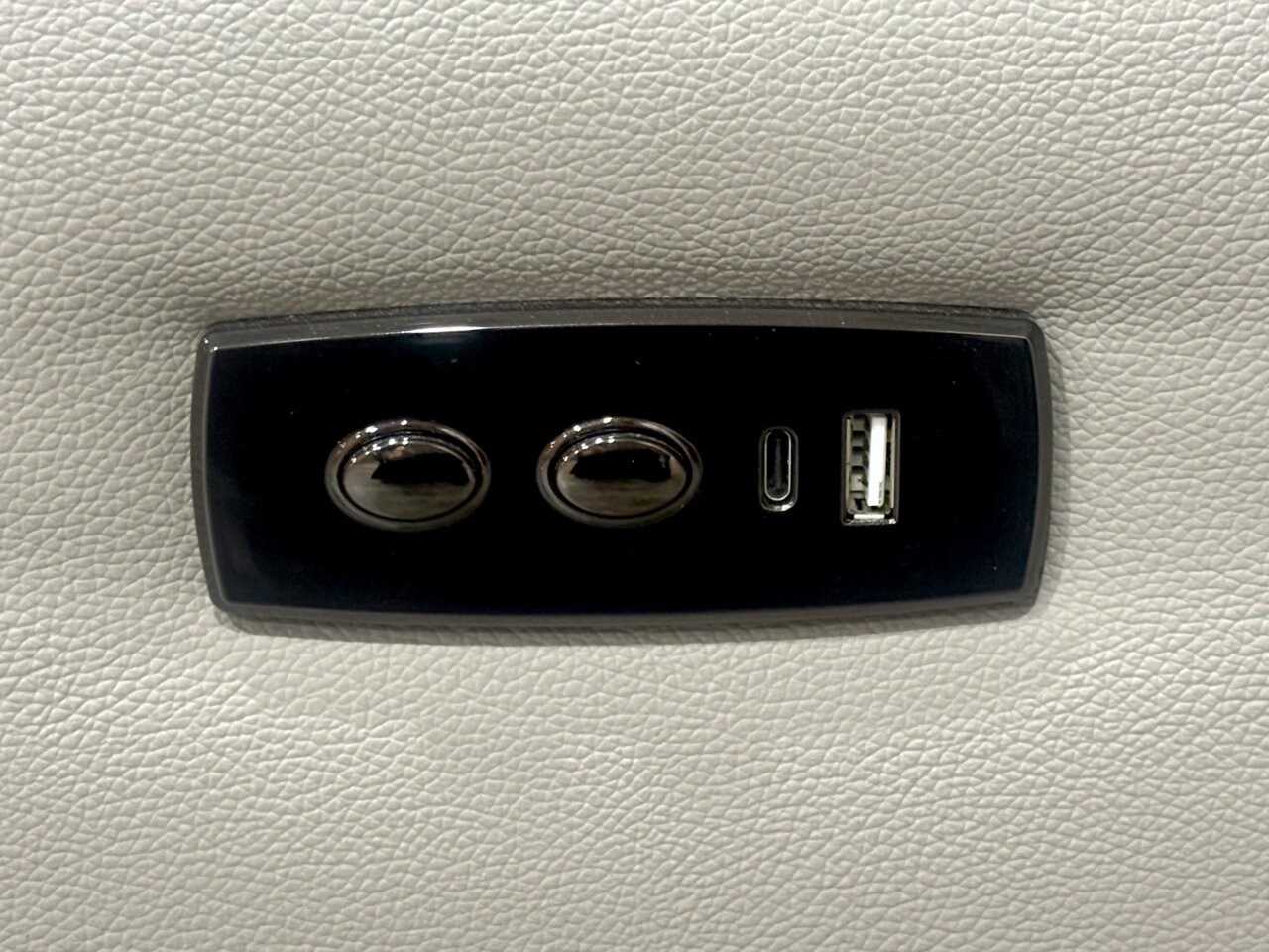 Nahaufnahme eines schwarzen Bedienfelds auf einem hellgrauen Sofa mit zwei Knöpfen und USB-Anschlüssen.