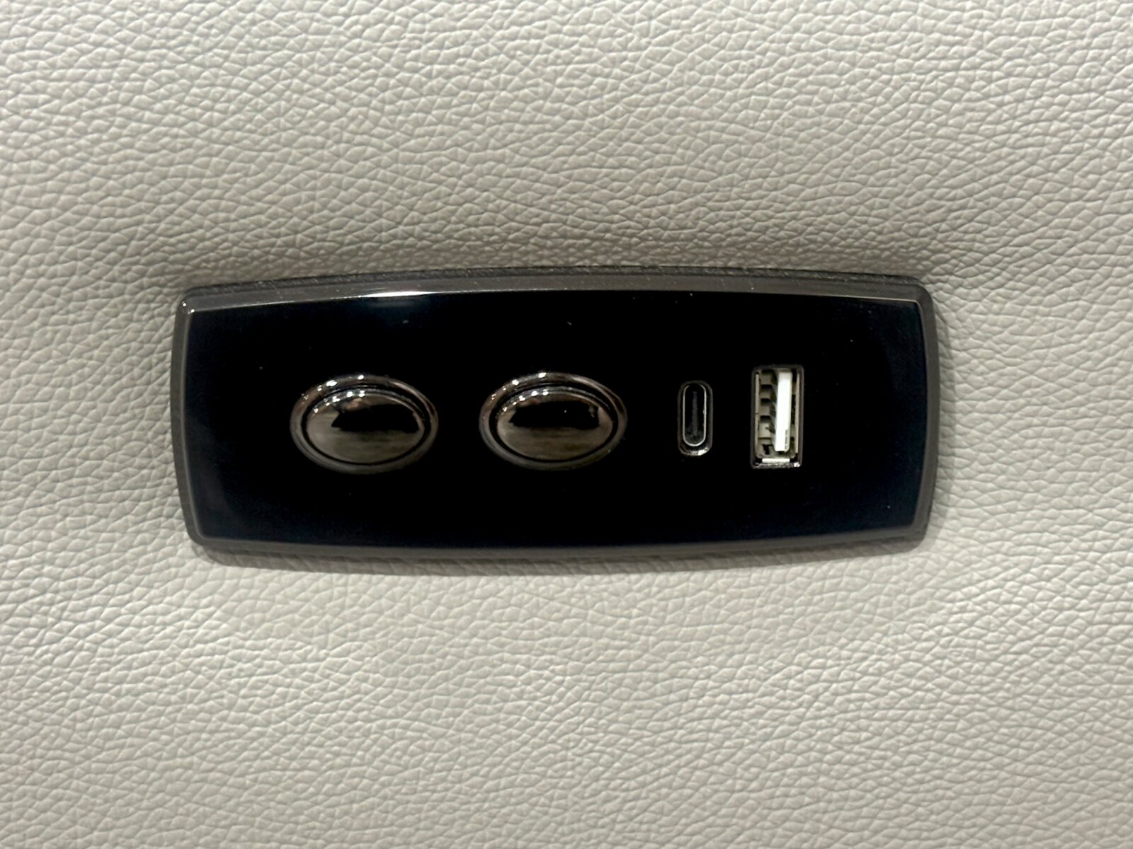 Nahaufnahme eines schwarzen Bedienfelds auf einem hellgrauen Sofa mit zwei Knöpfen und USB-Anschlüssen.