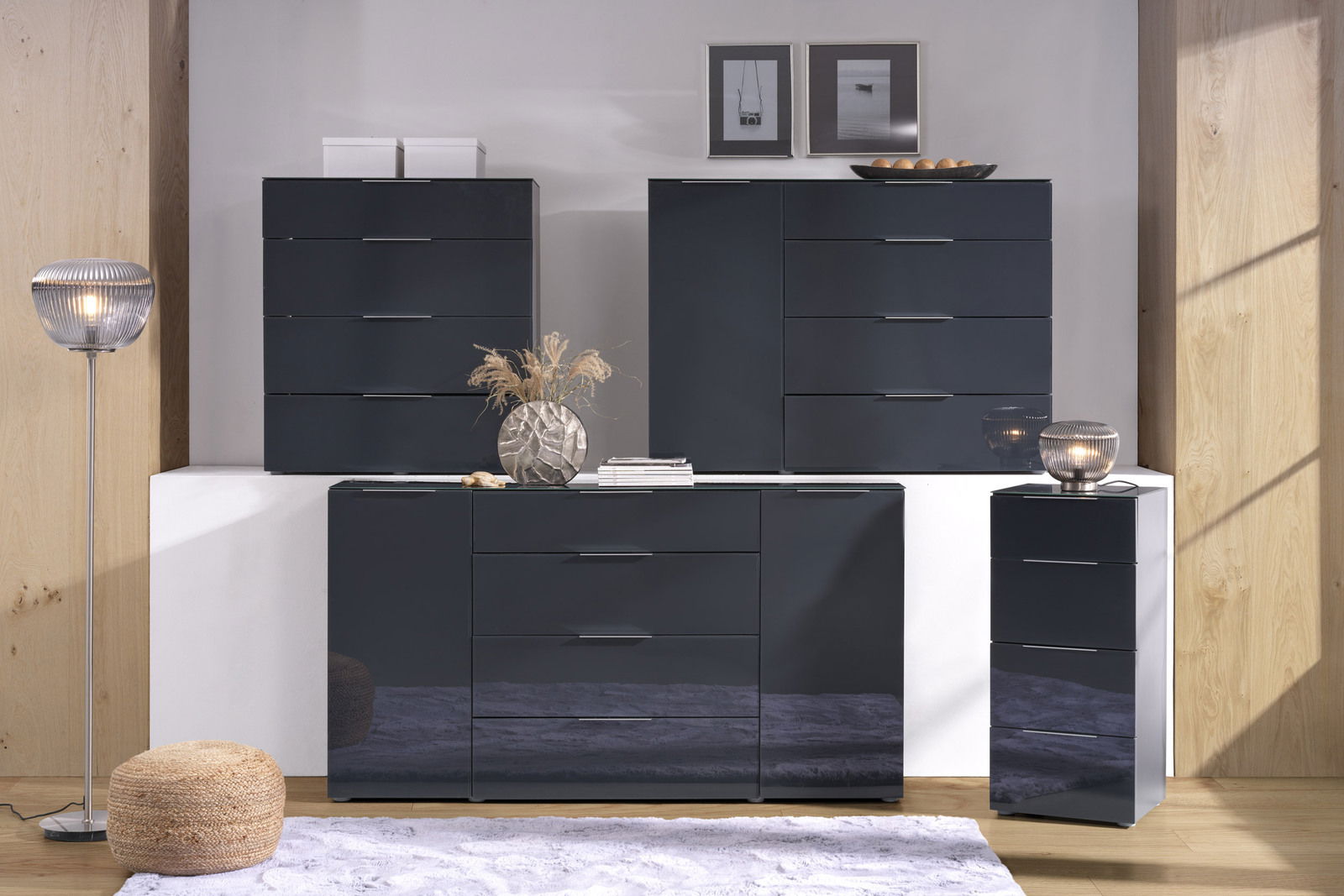 Voleo Hochkommode MALIN Moderne Hochkommode in dunklem Hochglanz-Finish, frontal fotografiert, umgeben von stilvoller Dekoration.