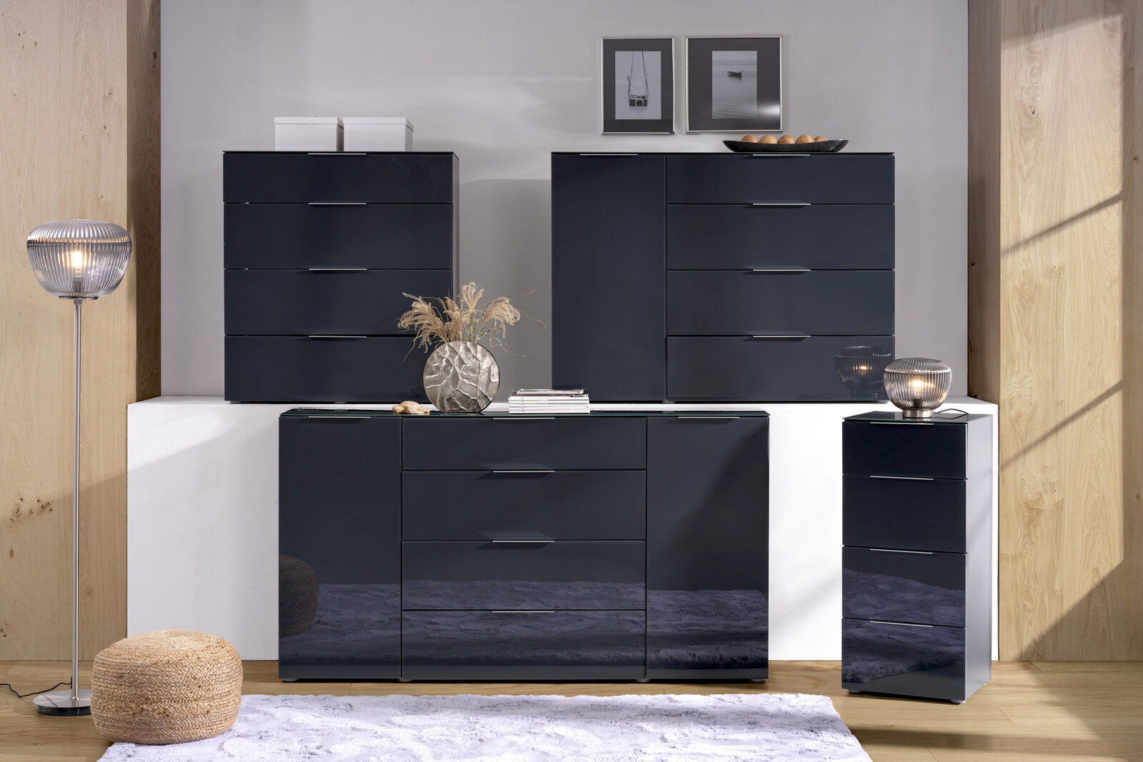 Voleo Hochkommode MALIN Moderne Hochkommode in dunklem Hochglanz-Finish, frontal fotografiert, umgeben von stilvoller Dekoration.