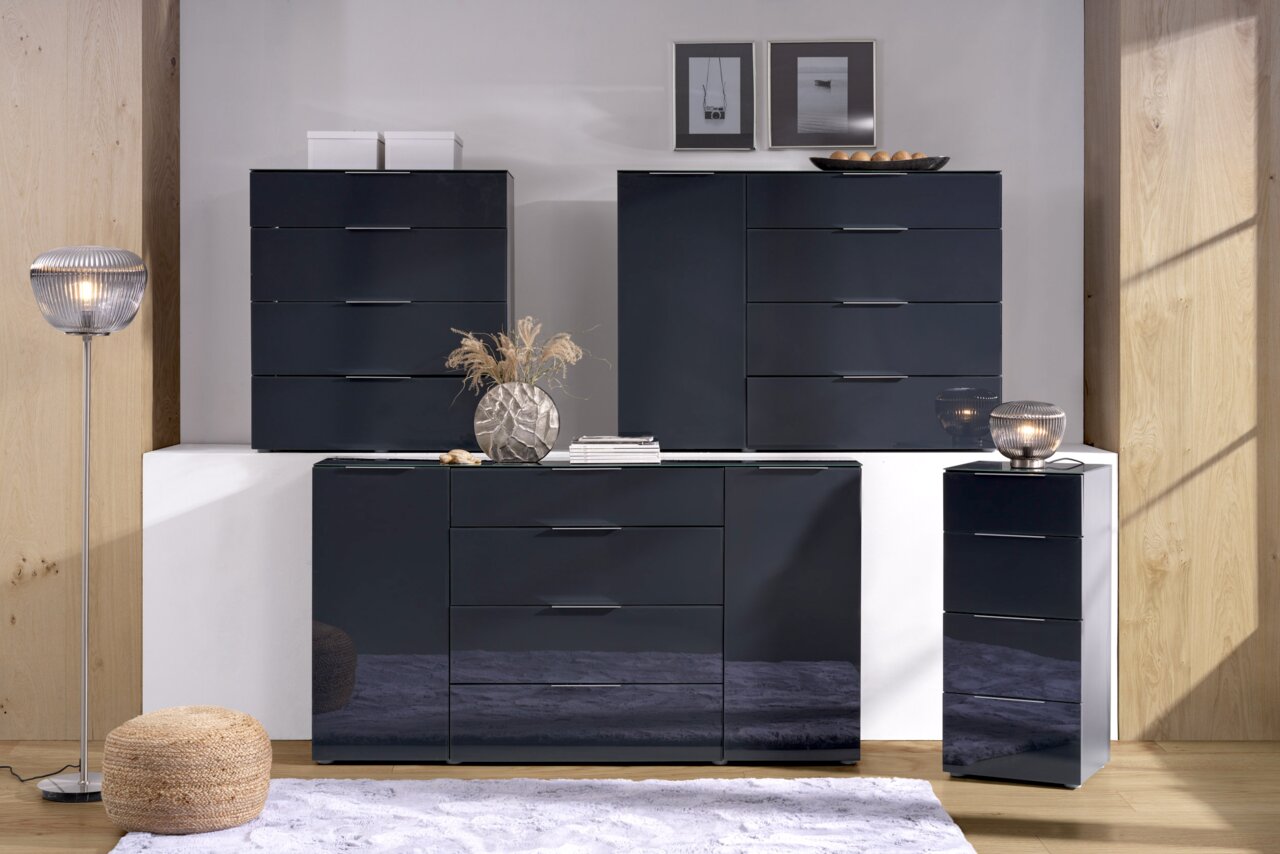 Voleo Hoge ladekast MALIN Moderne Hochkommode in dunklem Hochglanz-Finish, frontal fotografiert, umgeben von stilvoller Dekoration.