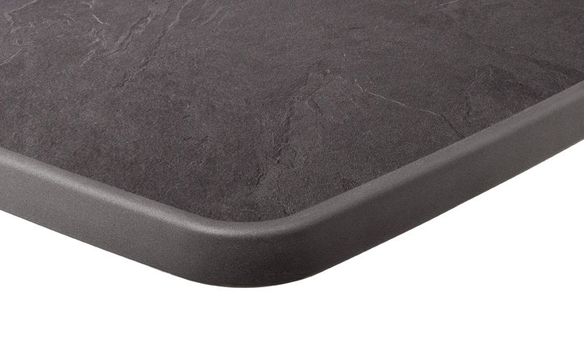 Nahaufnahme einer Tischkante in Graphitfarbe mit abgerundeten Ecken, perspektivisch von oben fotografiert.