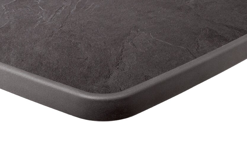 Nahaufnahme einer Tischkante in Graphitfarbe mit abgerundeten Ecken, perspektivisch von oben fotografiert.