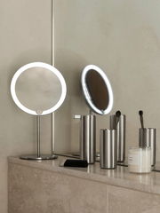 Moderner Seifenspender aus Edelstahl auf einem Badezimmerregal, umgeben von weiteren Badaccessoires. Perspektive von vorne.