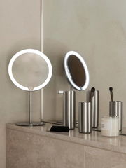 Moderner Seifenspender aus Edelstahl auf einem Badezimmerregal, umgeben von weiteren Badaccessoires. Perspektive von vorne.