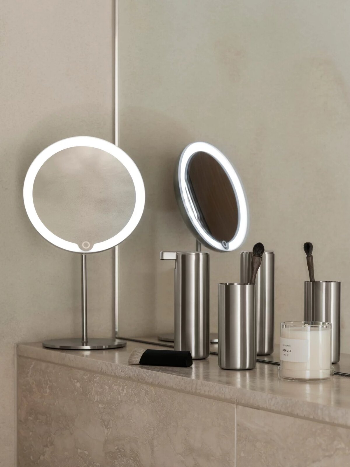 Moderner Seifenspender aus Edelstahl auf einem Badezimmerregal, umgeben von weiteren Badaccessoires. Perspektive von vorne.