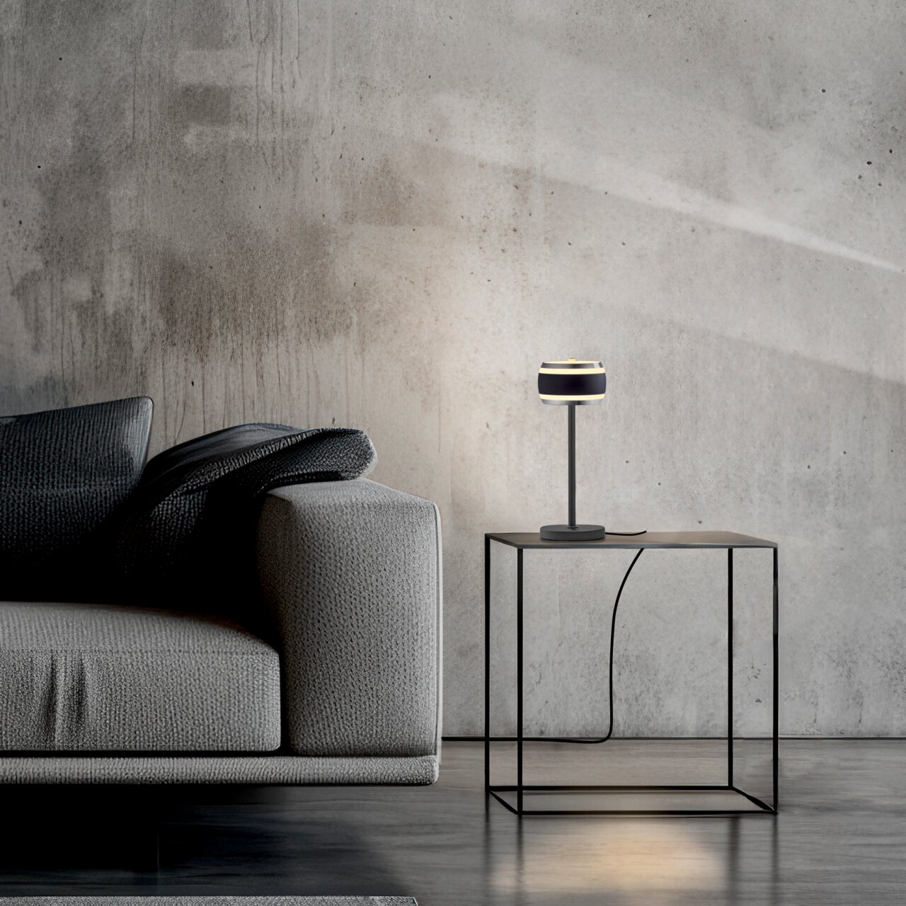 Neuhaus Pure Akku-Tischleuchte PURE FALLING RINGS Moderne Akku-Tischleuchte auf einem minimalistischen Beistelltisch neben einem grauen Sofa, seitliche Perspektive.