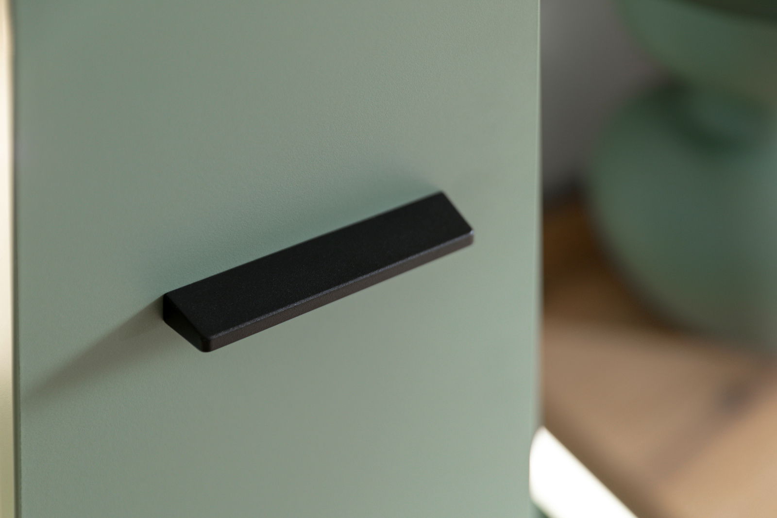 Nahaufnahme eines grünen Highboards mit schwarzem Griff, seitliche Perspektive