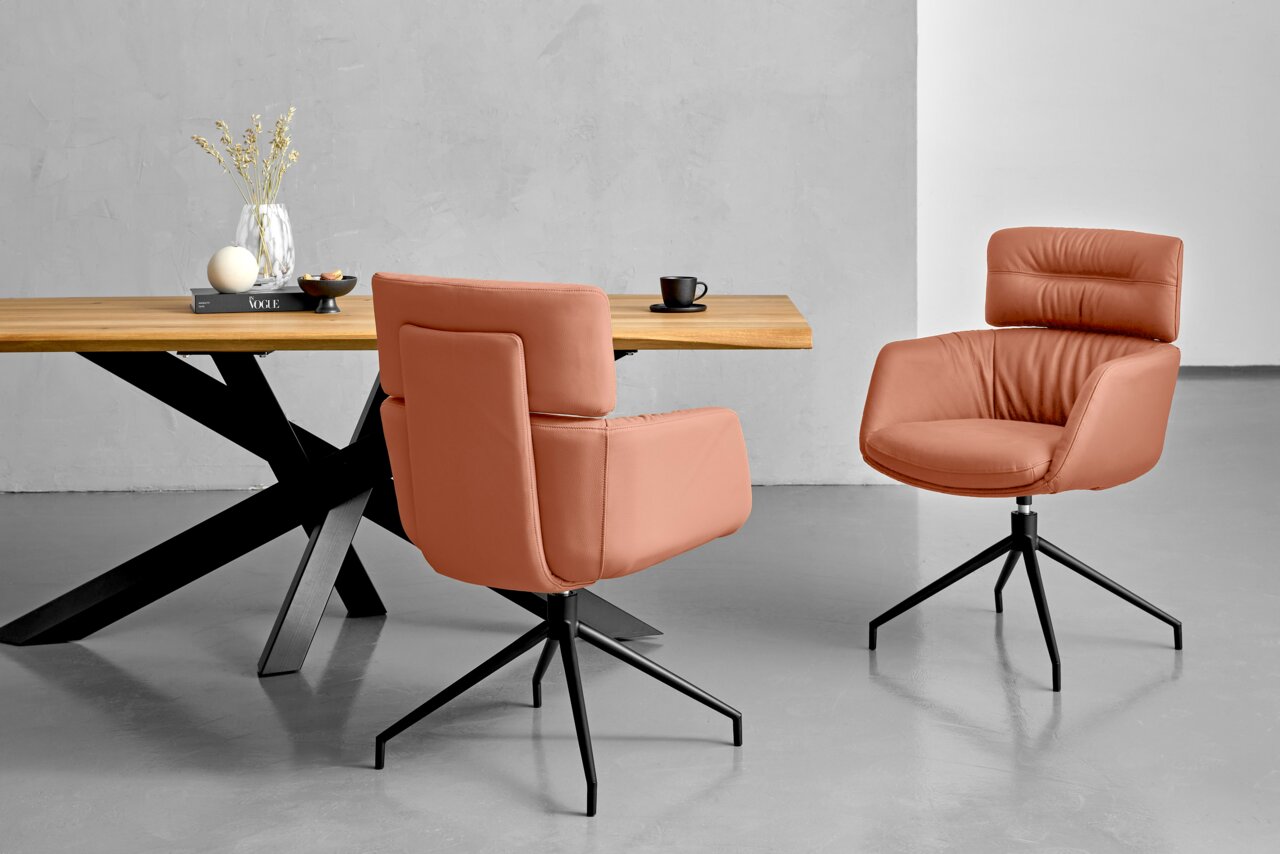 Dieter Knoll Fauteuil PABLO Twee moderne fauteuils in terracottakleur met een zwart metalen frame, gezien vanaf de zijkant, voor een houten tafel met decoratie.