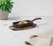 Grillpfanne mit Spaghetti und Basilikum auf einem Holzbrett, seitliche Perspektive