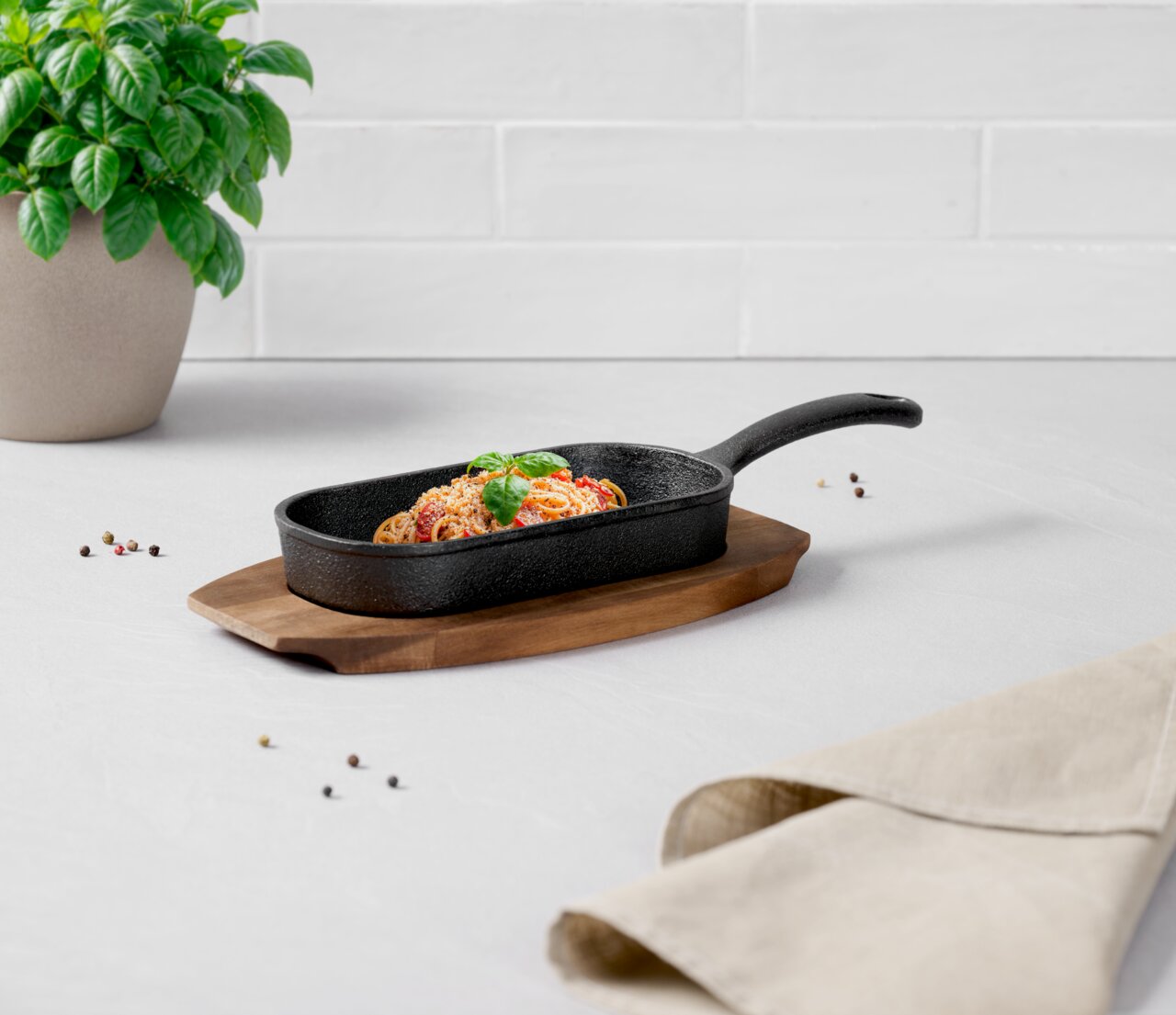 Grillpfanne mit Spaghetti und Basilikum auf einem Holzbrett, seitliche Perspektive