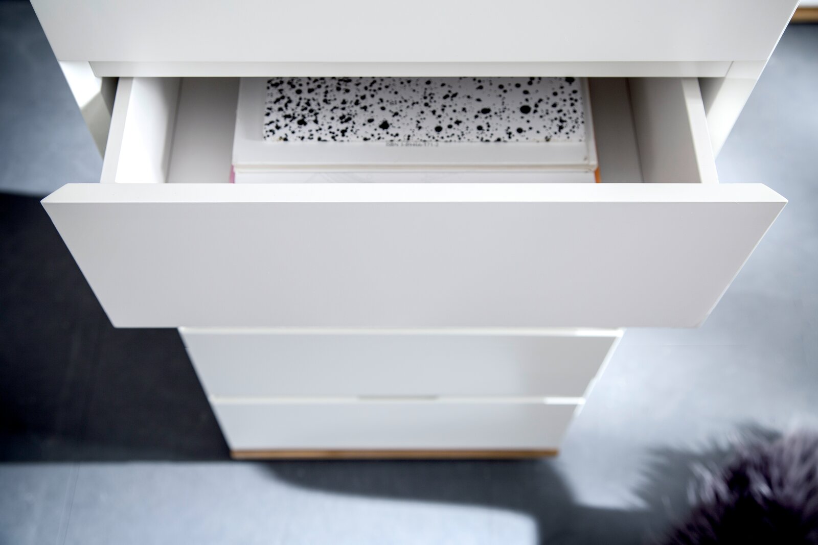 Nahaufnahme eines weißen Hochkommodenschublade mit geöffnetem Fach, von oben betrachtet, mit einem Buch im Inneren.