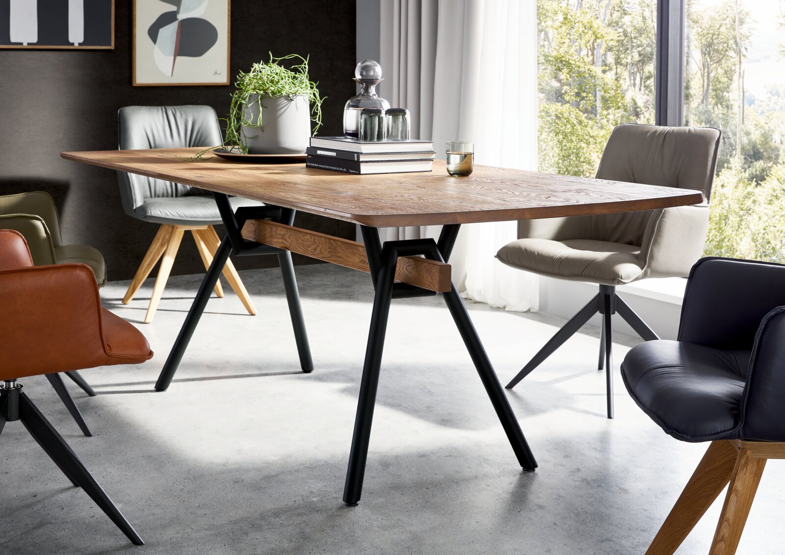 Moderne rechthoekige houten eettafel met zwart metalen A-poten in een lichte eetkamer, schuin van voren gefotografeerd met stoelen eromheen