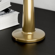 Close-up van de ronde voet van een goudkleurige metalen tafellamp op een zwart tafelblad, licht van bovenaf en van opzij gezien