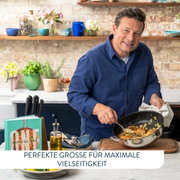 Jamie Oliver in einer Küche, hält eine Servierpfanne mit Essen in der Hand, seitliche Perspektive.