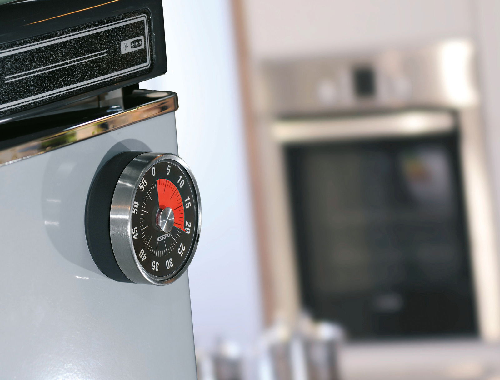 Mechanischer Küchentimer in Nahaufnahme, seitlich an einem Gerät befestigt, mit rotem und schwarzem Ziffernblatt.