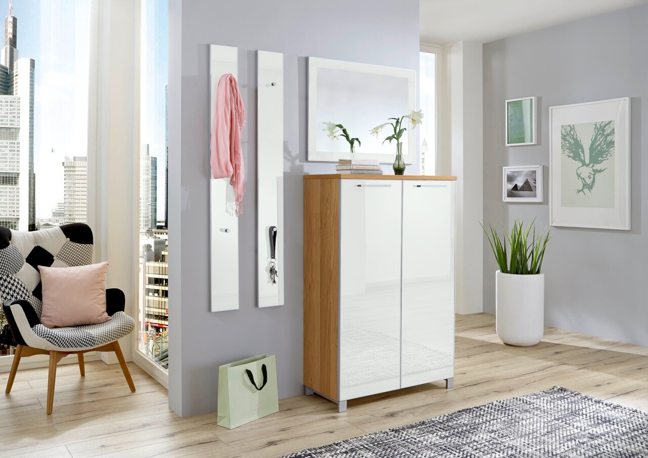 Modernes Garderoben-Set in einem hellen Raum mit Stadtblick, bestehend aus einem Schrank mit Holz- und weißen Elementen, zwei schmalen Wandpaneelen mit Haken und einem Spiegel. Perspektive von vorne.